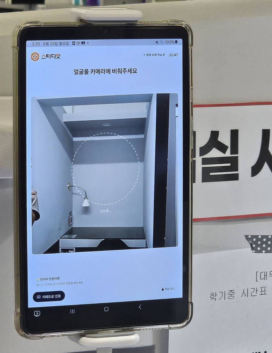거치대에 세워진 안면인식 체크인 태블릿 — '얼굴을 카메라에 비춰주세요' 화면